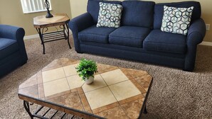 A living room with a dark blue sofa, two patterned throw pillows, a small side table with a lamp, and a coffee table with a plant. - 3-bedroom condo in welcoming Kissimmee with WiFi, AC and Gated community. (Kissimmee)