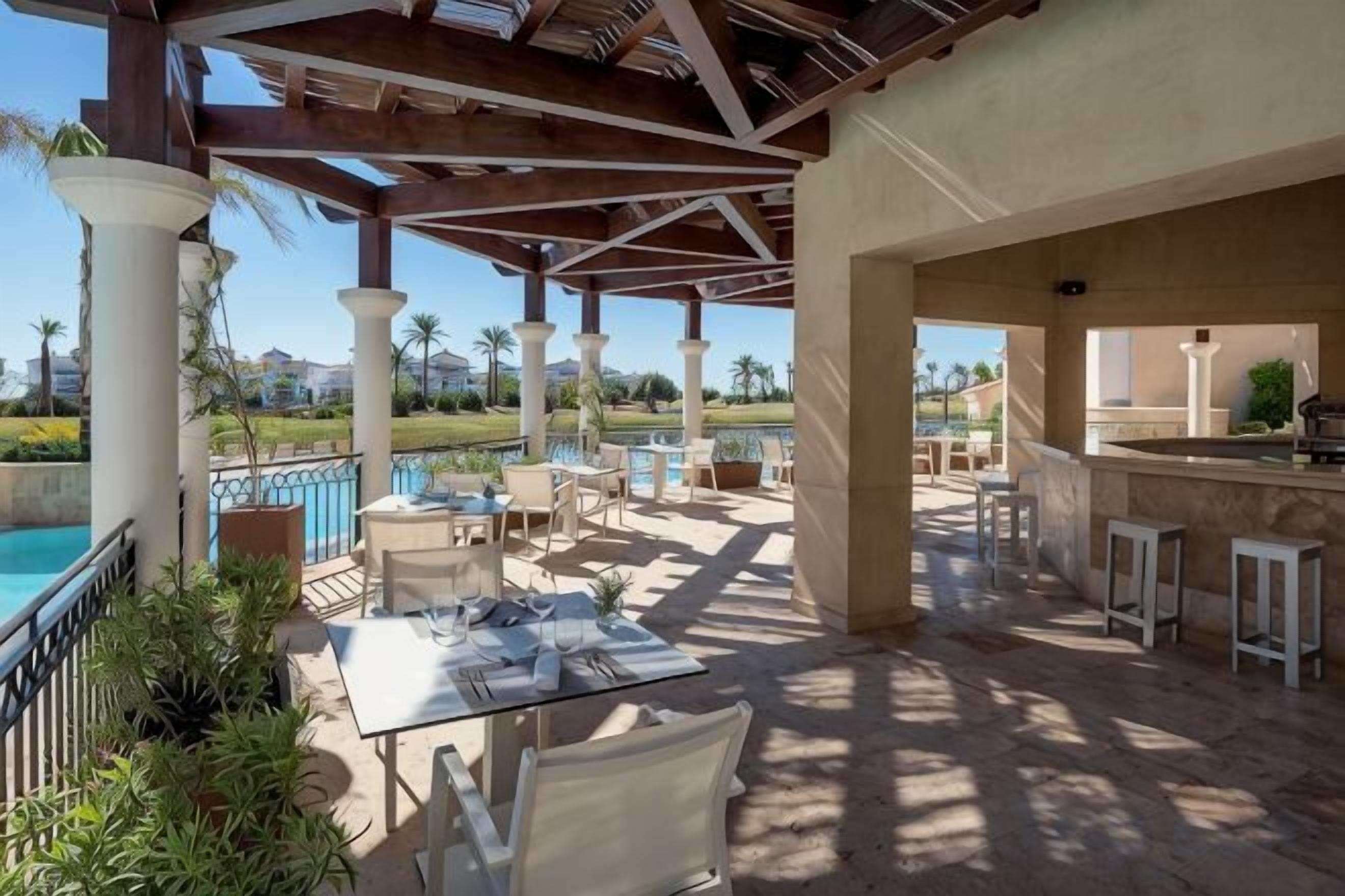 Un patio exterior con mesas y sillas, una piscina y una zona de bar.