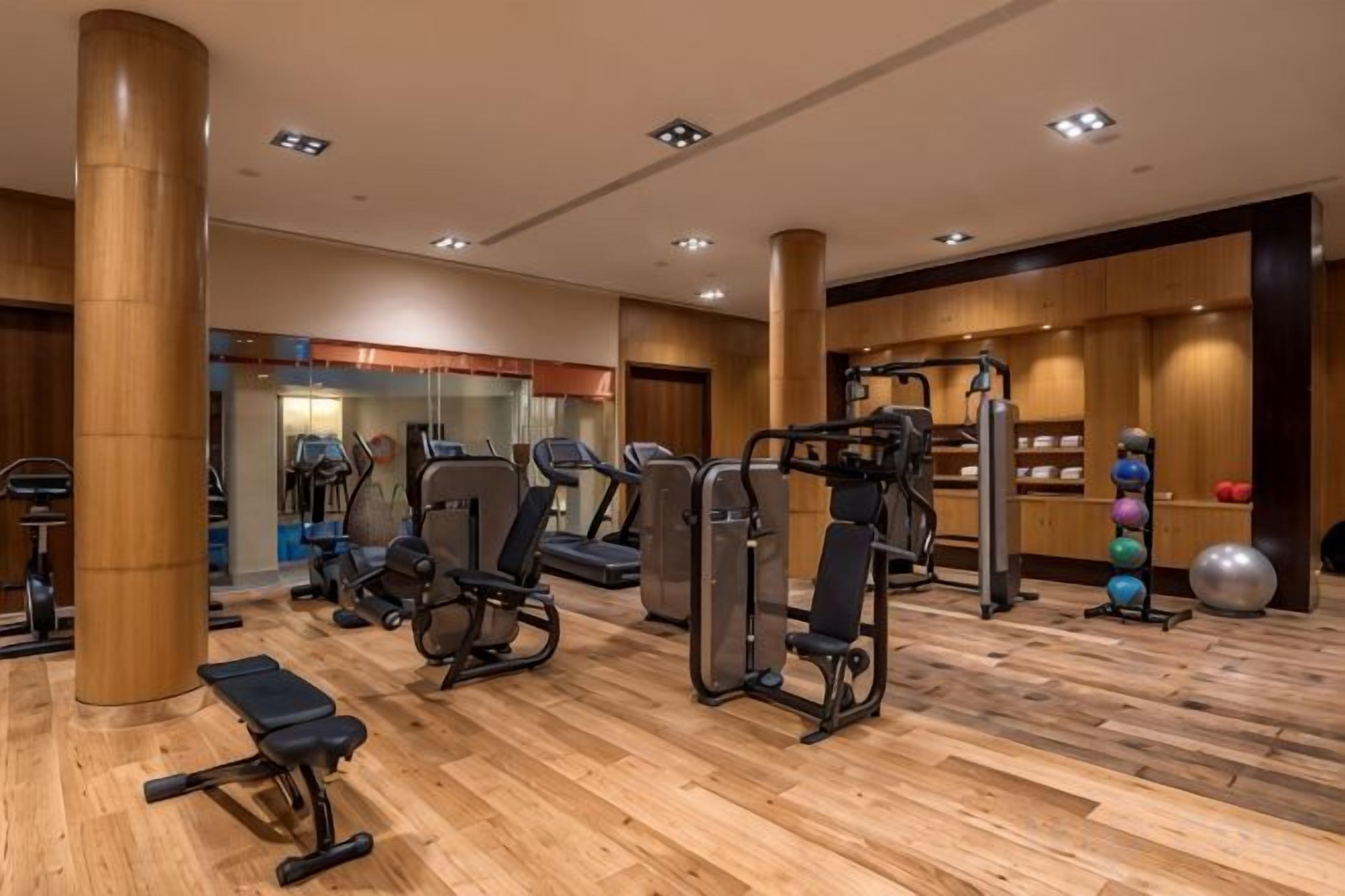 A gym with exercise equipment, wooden flooring, and a wall with exercise balls.