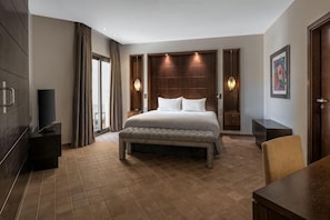 A hotel room with a large bed, a bench, a TV, a desk, and a door. - DoubleTree by Hilton La Torre Golf & Spa Resort (Murcia)