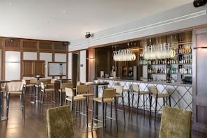 A bar area with high stools, a bar counter, and a well-stocked liquor shelf. - DoubleTree by Hilton La Torre Golf & Spa Resort (Murcia)