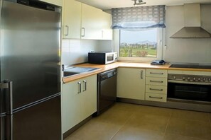 A kitchen with a stainless steel refrigerator, microwave, oven, and a window with a view. - DoubleTree by Hilton La Torre Golf & Spa Resort (Murcia)
