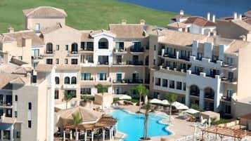 Un resort con varias edificaciones, una piscina central y vista al mar.