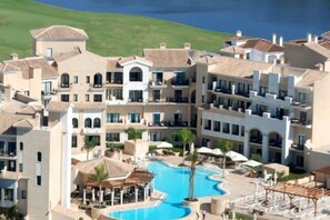 Un resort con varias edificaciones, una piscina central y vista al mar.