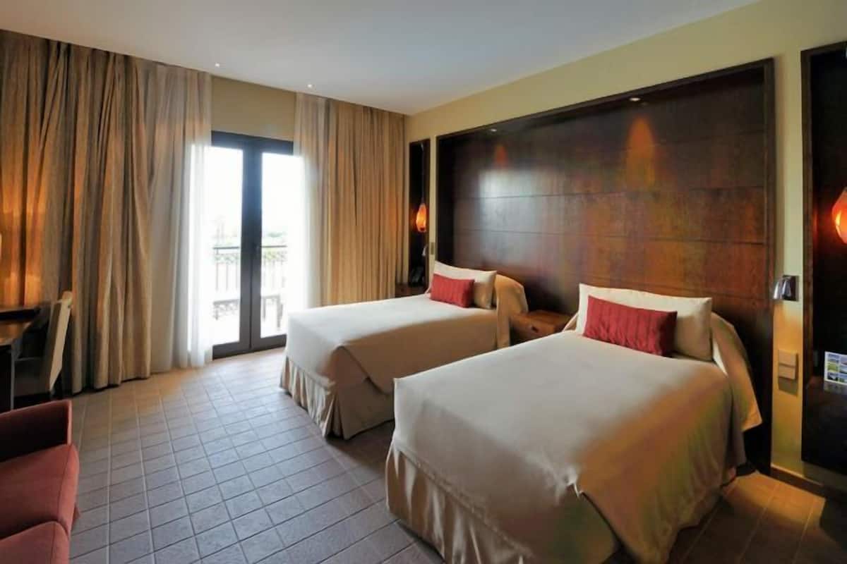 A hotel room with two beds, a large window, and a view of the outdoors.