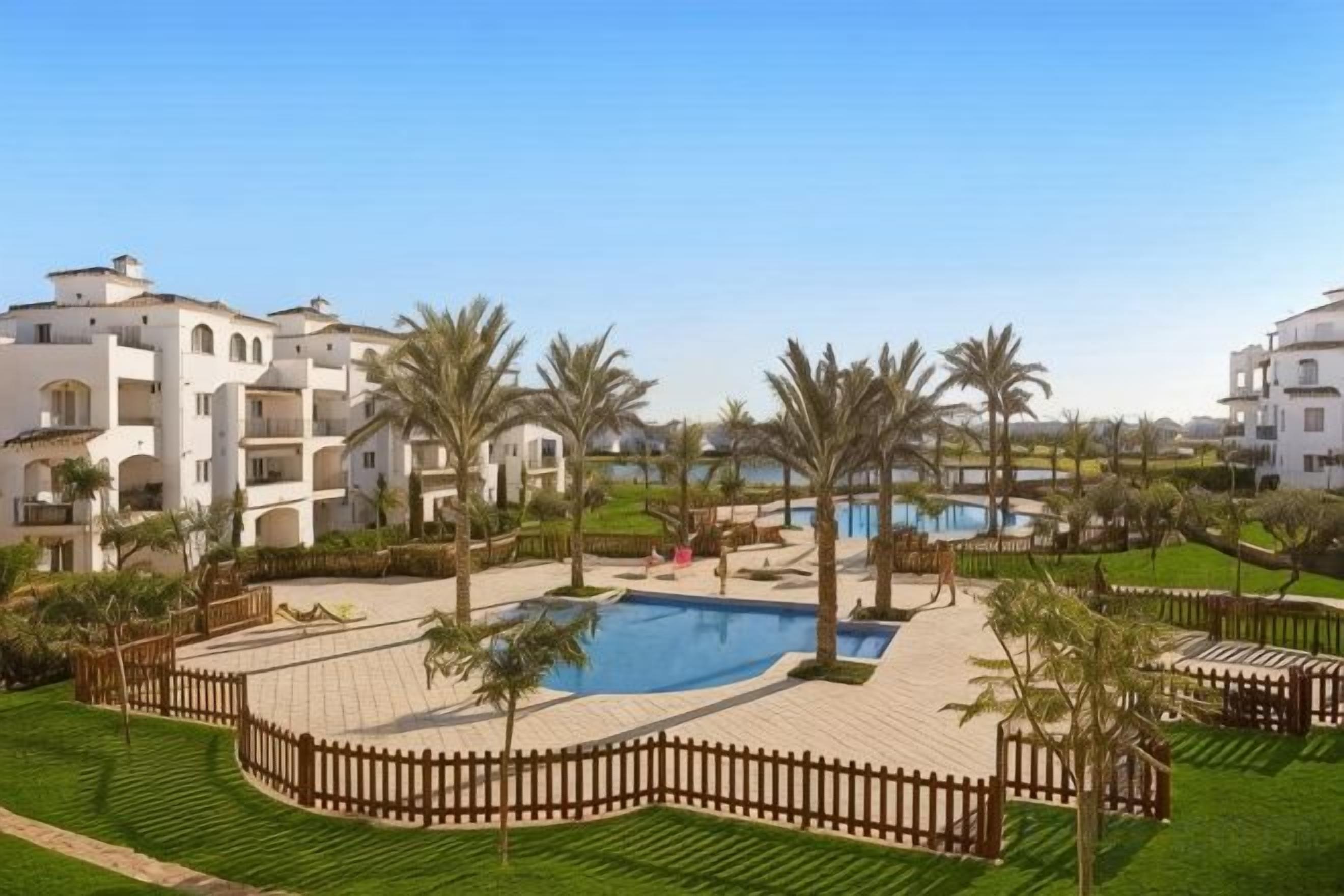 Un resort con piscina, palmeras y un área cercada.