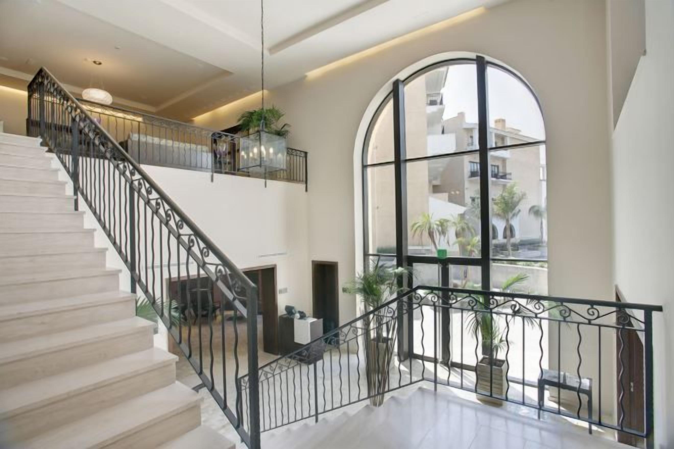Un interior espacioso con una escalera, ventanas grandes y plantas de interior.