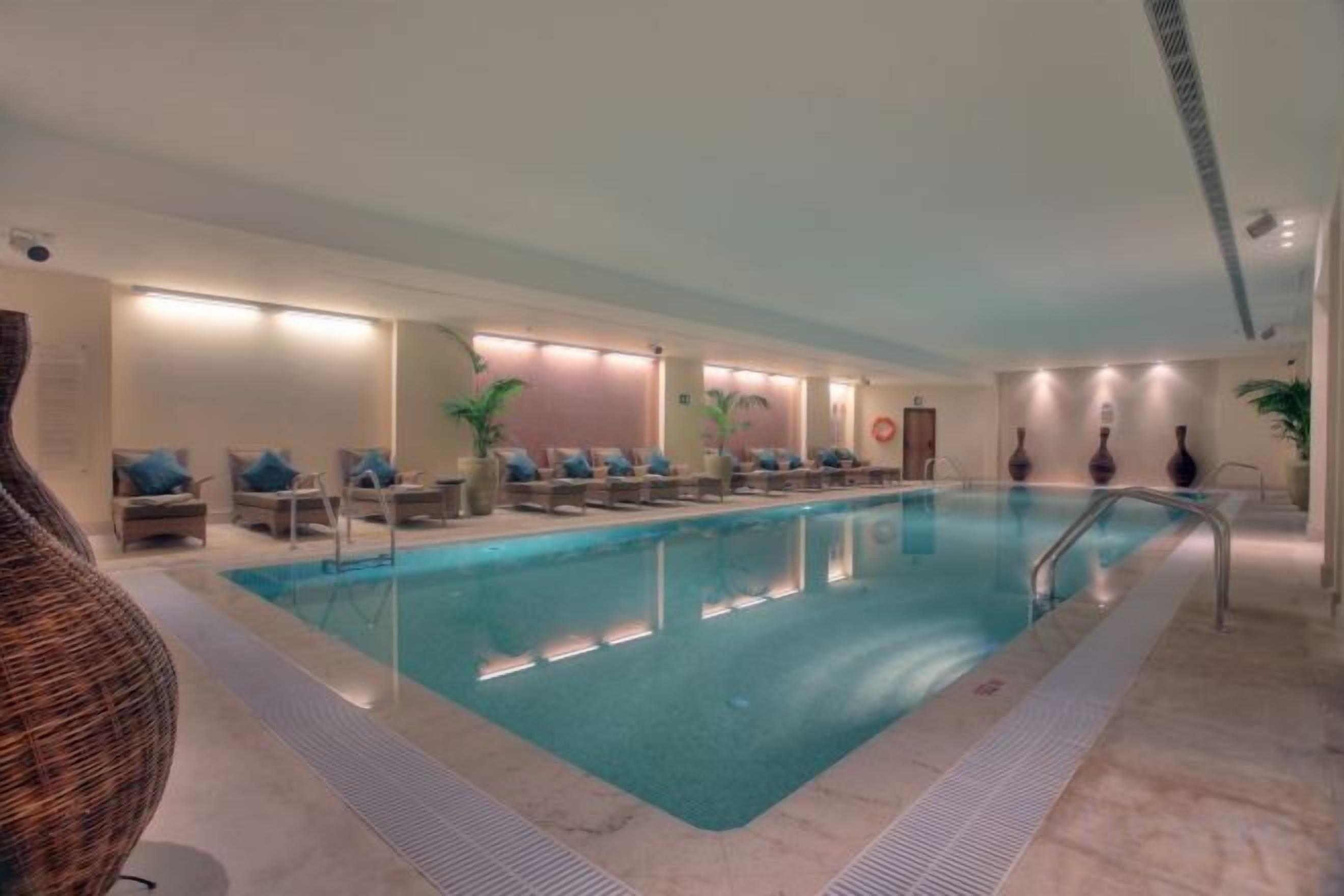 Una piscina interior con sillas de descanso y un largo banco a un lado.