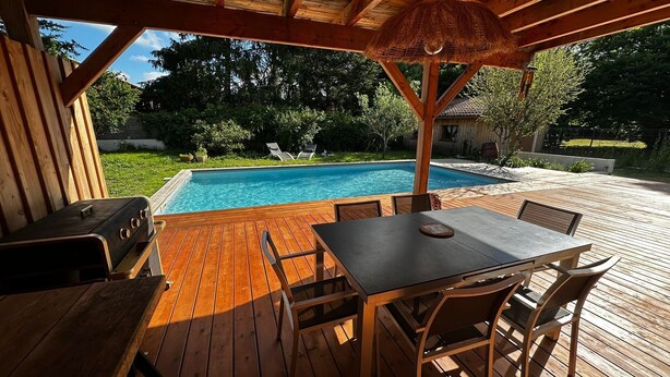 A wooden deck with a pool, outdoor seating, and a grill.