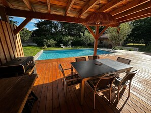 A wooden deck with a pool, outdoor seating, and a grill. - House with a pool on the edge of the Arcachon Basin. (Biganos)