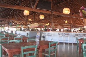 A restaurant with wooden tables and chairs, a bar area, and hanging pendant lights. - hu Park Albatros Village (San Vincenzo)