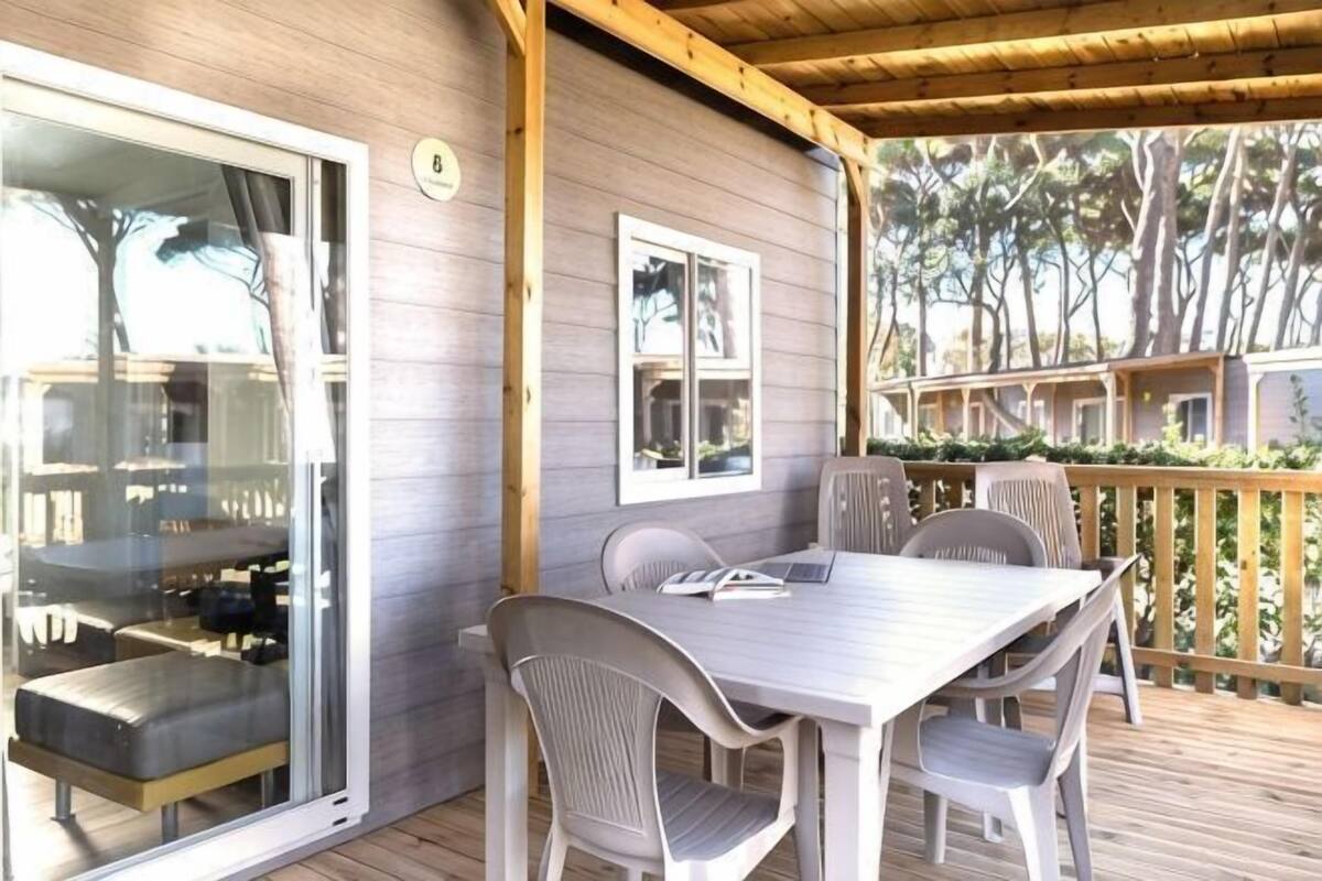 Uma área externa coberta com mesa, cadeiras, uma porta de vidro deslizante e um deck de madeira.