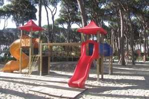 A playground with a slide and climbing structures, surrounded by trees. - hu Park Albatros Village (San Vincenzo)