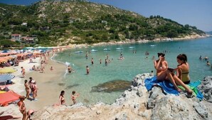 Une plage avec des gens, des bateaux et une côte rocheuse.
