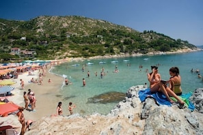 Una playa con gente, barcos y un litoral rocoso.