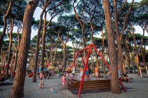 Un parque infantil con columpios y estructuras para escalar, rodeado de árboles.