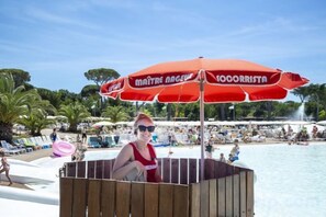Escena de playa con una estructura de madera, una sombrilla roja y una piscina.