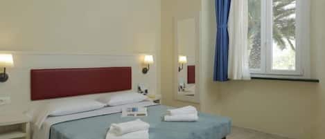 Habitación de hotel con cama, mesitas de noche, lámparas, una ventana con cortinas y vistas a palmeras.