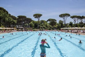 Une grande piscine extérieure dotée de plusieurs couloirs de nage, entourée d’arbres et de chaises longues.