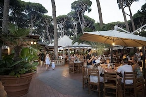 An outdoor dining area with tables and chairs, surrounded by large umbrellas and potted plants. - hu Park Albatros Village (San Vincenzo)