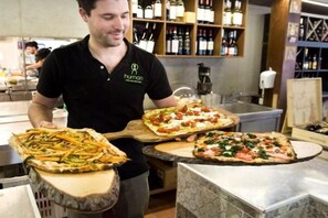 Une personne tenant trois pizzas sur des planches en bois, dans une cuisine.