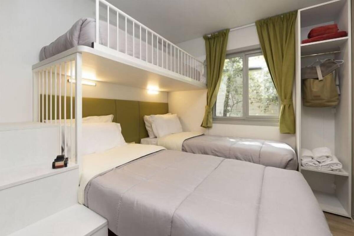 Quarto com duas camas, incluindo uma beliche, um guarda-roupa e uma janela com cortinas.