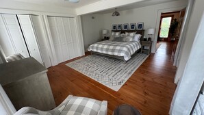 Een slaapkamer met een bed, bureau, stoel, plafondventilator en een gang naar een andere kamer.
