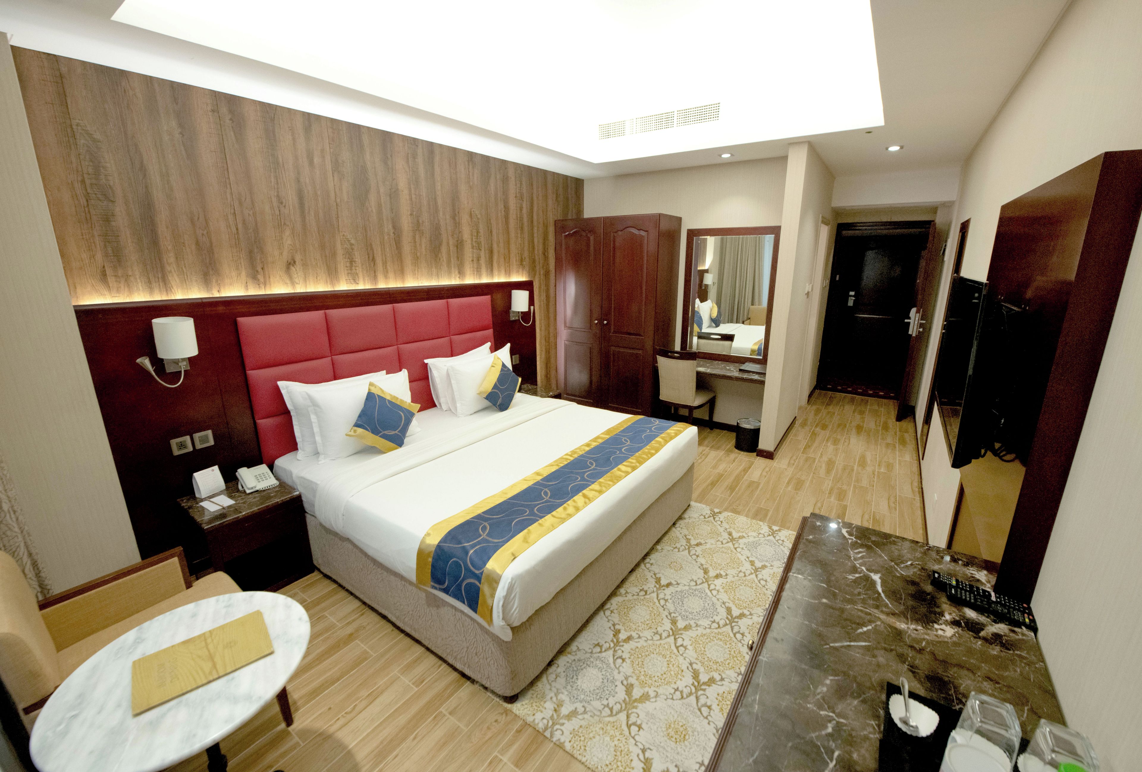 A hotel room with a large bed, a desk, a chair, a mirror, and a wardrobe.