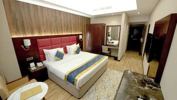 A hotel room with a large bed, a desk, a chair, a mirror, and a wardrobe.