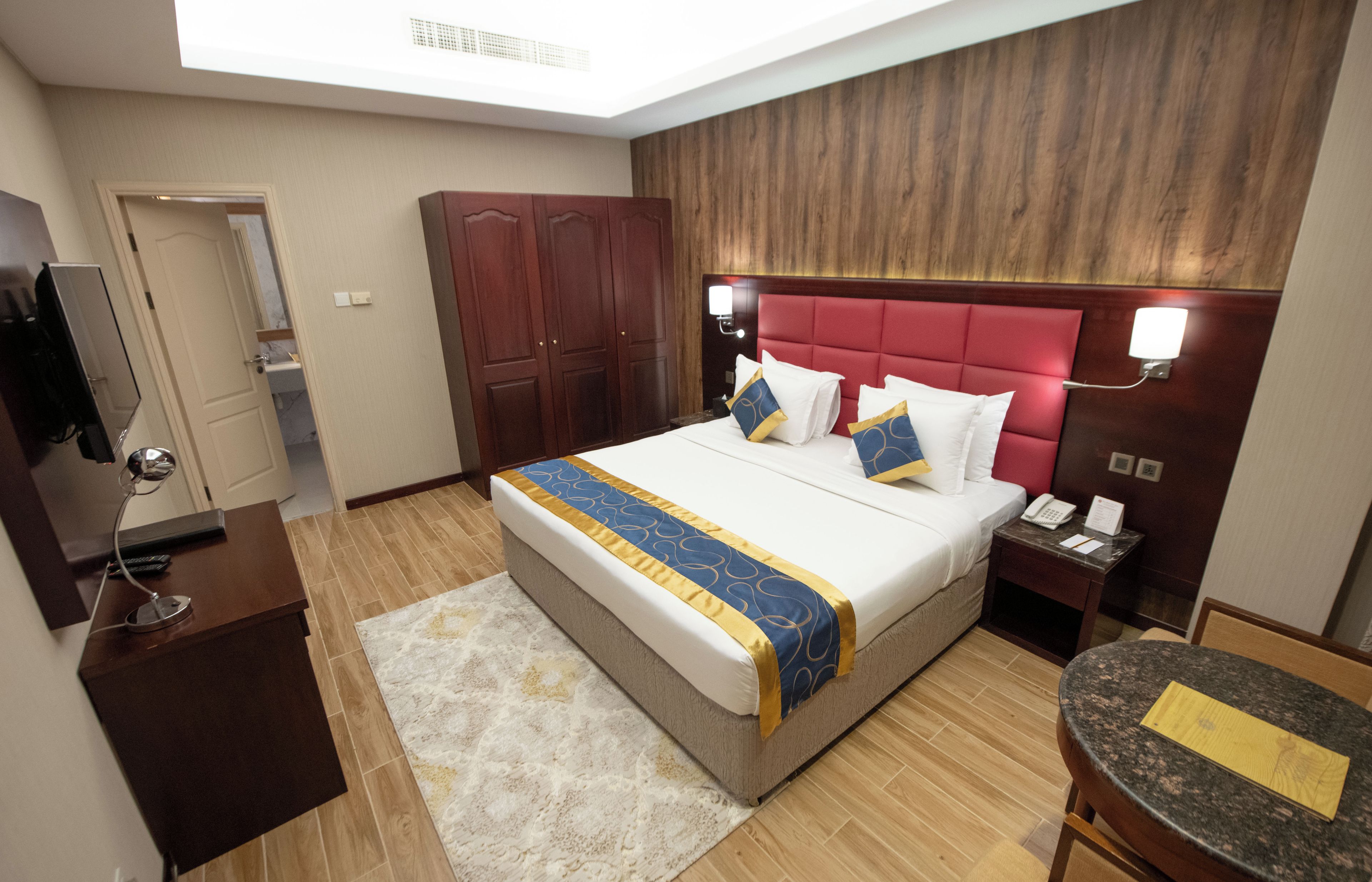 Una habitación de hotel con cama, escritorio, televisor, armario y puerta de baño.
