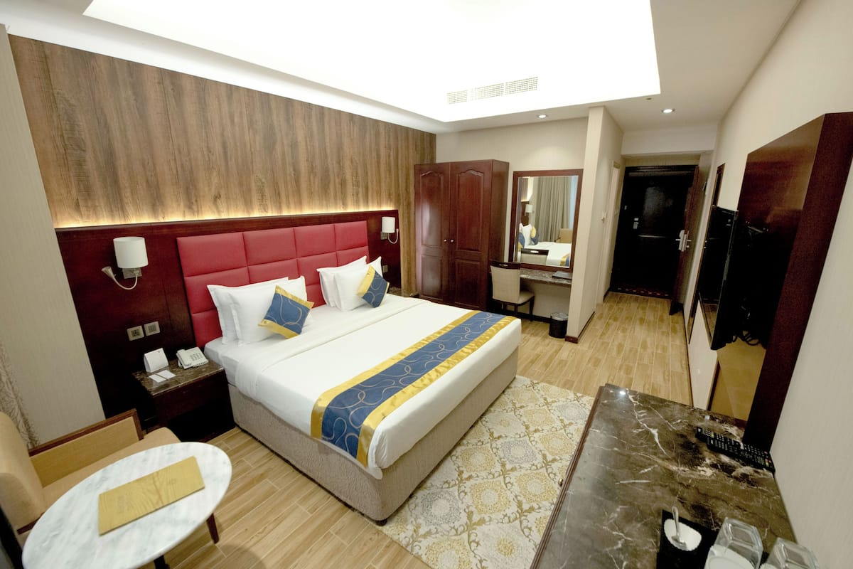 Una habitación de hotel con una cama grande, un escritorio, una silla, un espejo y un armario.