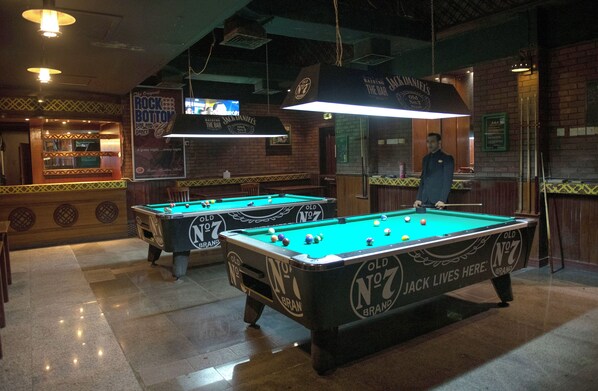 A billiards room with two pool tables, a television, and a brick wall. - Ramee Guestline Hotel (Muscat)