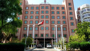 A large hotel with a symmetrical facade, multiple windows, and a flag. - Ramee Guestline Hotel (Muscat)