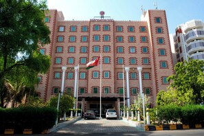 A large hotel with a symmetrical facade, multiple windows, and a flag. - Ramee Guestline Hotel (Muscat)