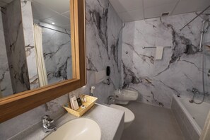 A bathroom with a marble wall, a sink, a toilet, and a bathtub. - Ramee Guestline Hotel (Muscat)