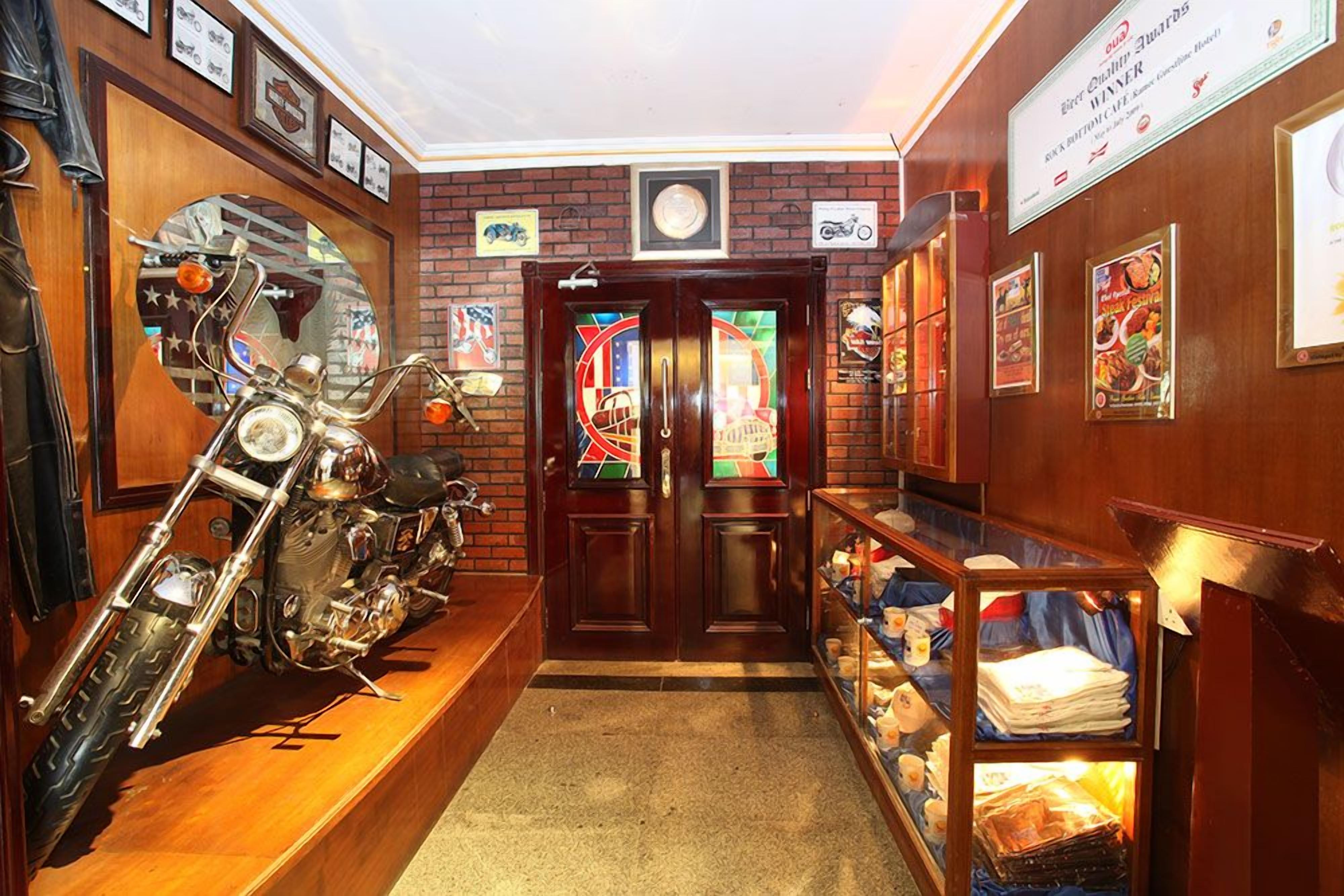 A hallway with a motorcycle on display, a wooden reception desk, and a wall with framed awards.