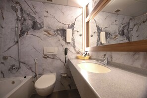 Un baño con pared de mármol, una bañera, un inodoro, un lavabo con espejo y un perchero para toallas.