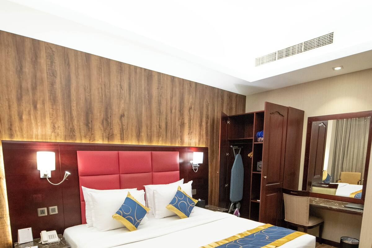 Una habitación de hotel con una cama grande, cabecera de madera, mesita de noche con teléfono y un espejo.
