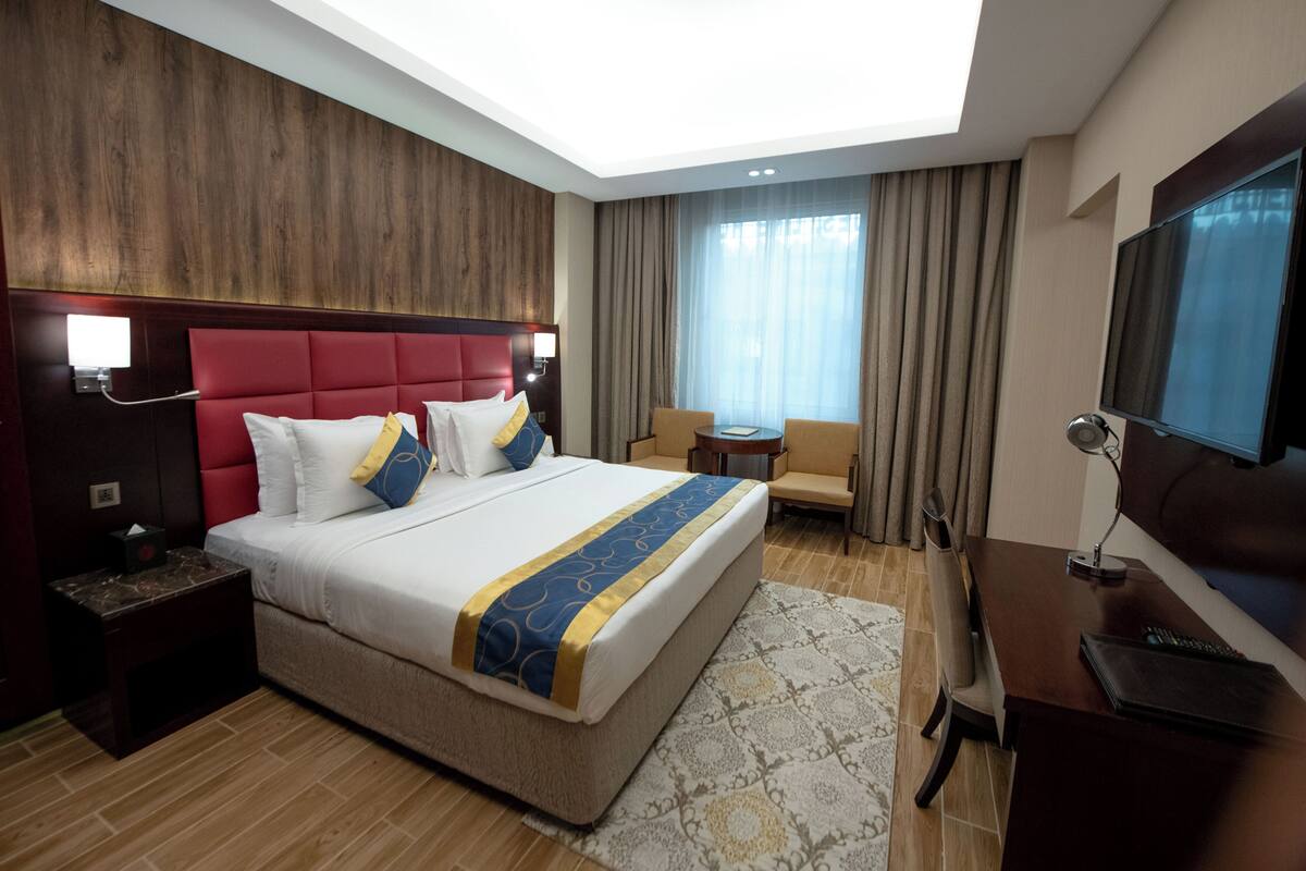 Habitación de hotel con una cama grande, un escritorio, un televisor y una zona de estar con vistas al exterior.