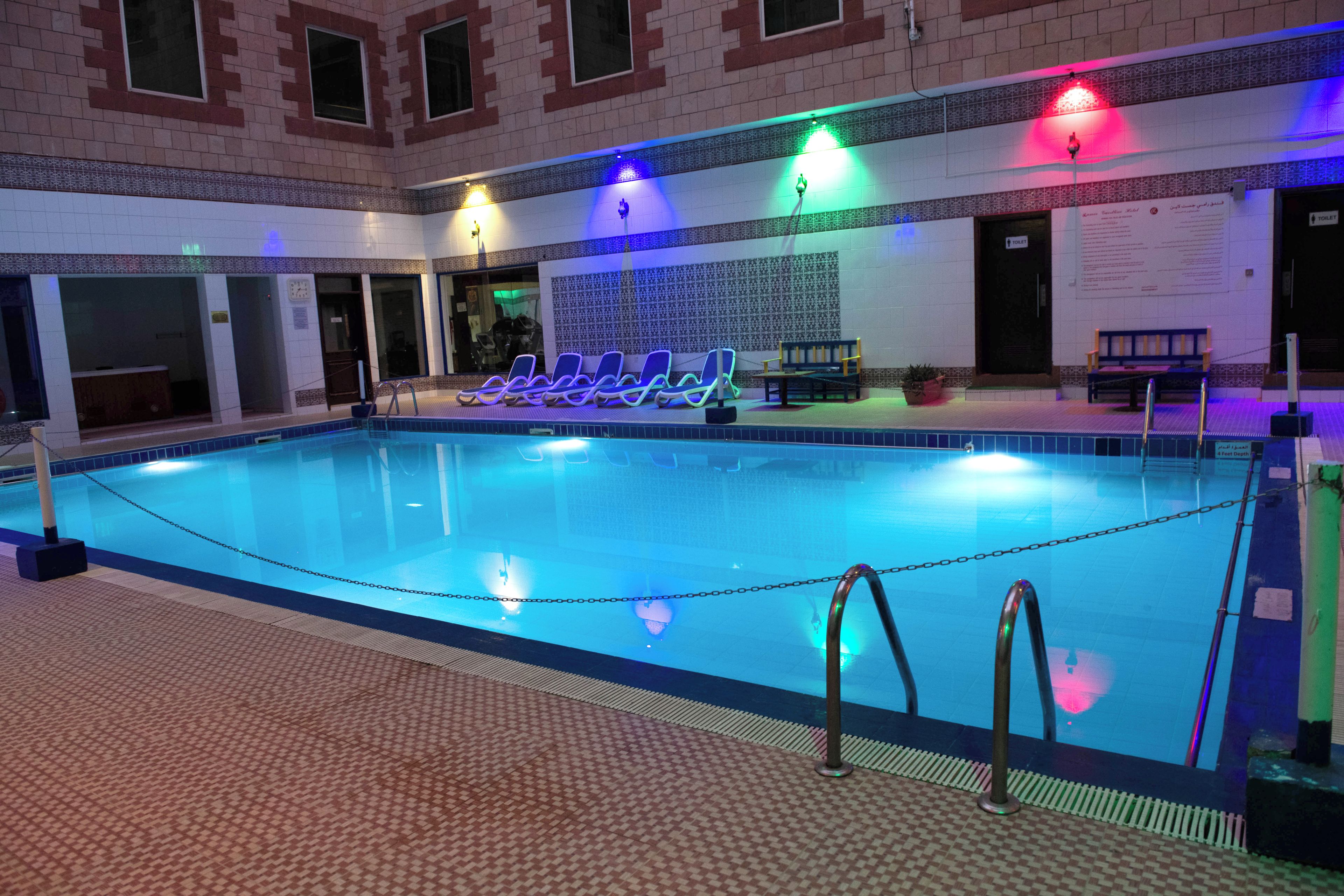 Una piscina interior con suelo de baldosas, sillas de descanso y un banco.