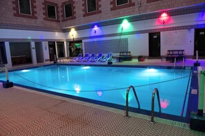 En indendørs swimmingpool med flisegulv, liggestole og en bænk.