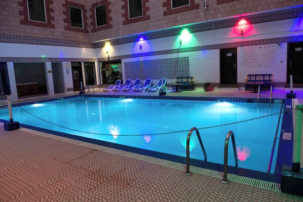 An indoor swimming pool with a tiled floor, lounge chairs, and a bench. - Ramee Guestline Hotel (Muscat)