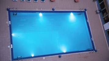 A rectangular swimming pool with a blue border, surrounded by a tiled deck.