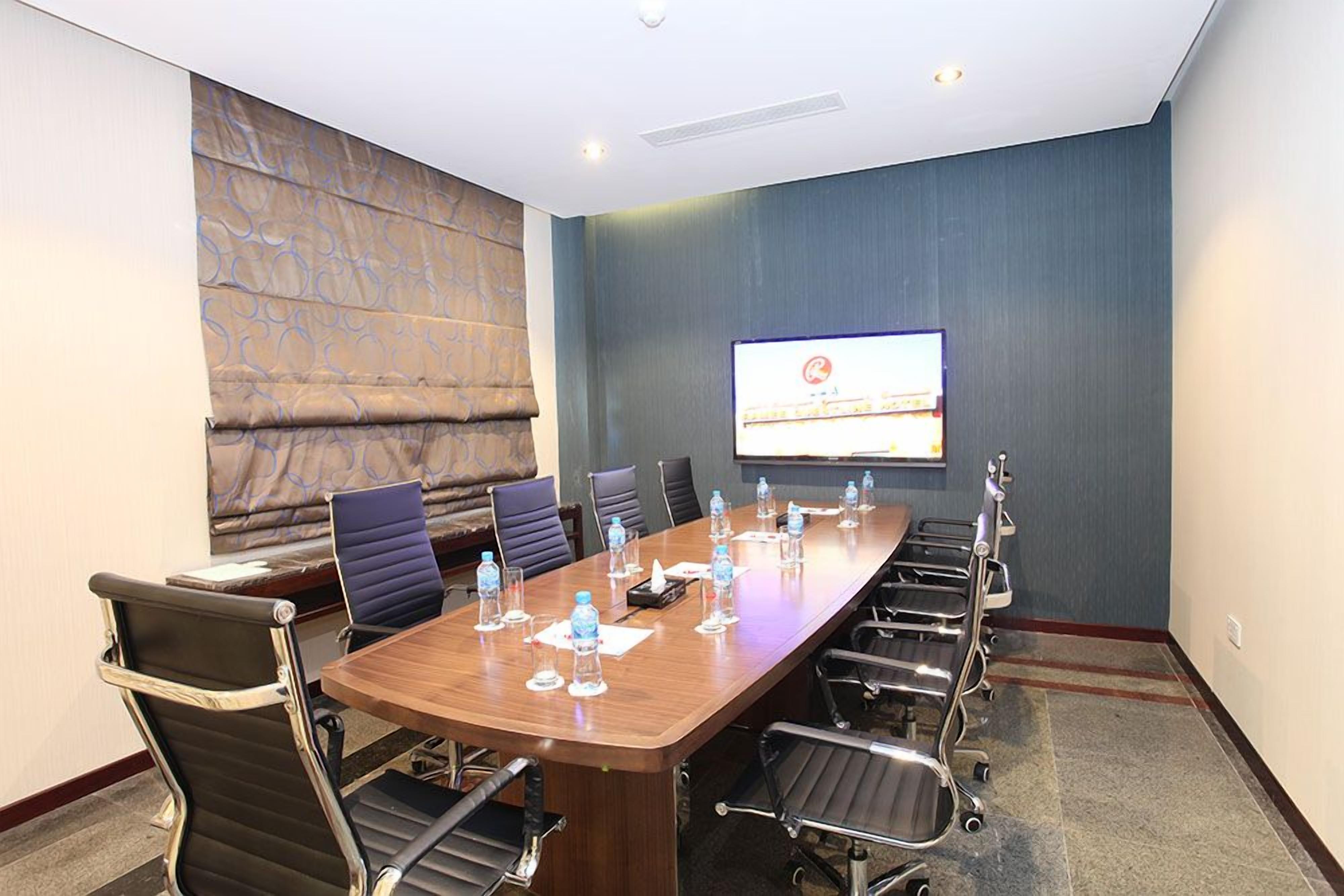 Un salón de conferencias con una larga mesa, sillas, botellas de agua y una pantalla para proyector.