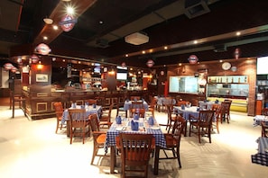 Un restaurante con varias mesas y sillas, una zona de bar y una barra con una pantalla de menú.