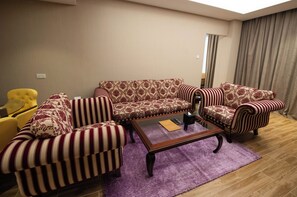 A living room with a patterned sofa, striped armchairs, a coffee table, and a yellow armchair. - Ramee Guestline Hotel (Muscat)