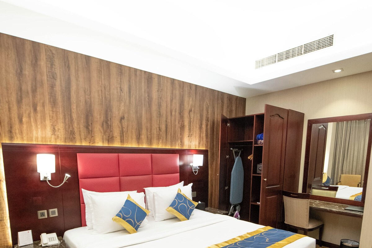Ein Hotelzimmer mit einem großen Bett, einem Holzkopfteil, einem Nachttisch mit Telefon und einem Spiegel.