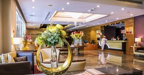 Un hall de hotel con una recepción, área de descanso y un jarrón decorativo con flores.