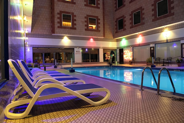 Una piscina con sillas de descanso, piso de baldosas y un edificio con fachada ornamentada.