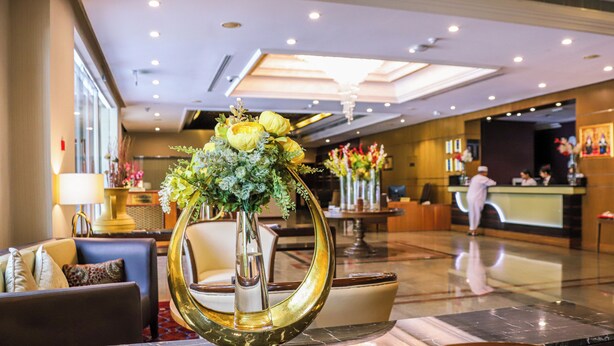 Un hall d’hôtel comprenant un comptoir d’accueil, un espace salon et un vase décoratif orné de fleurs.